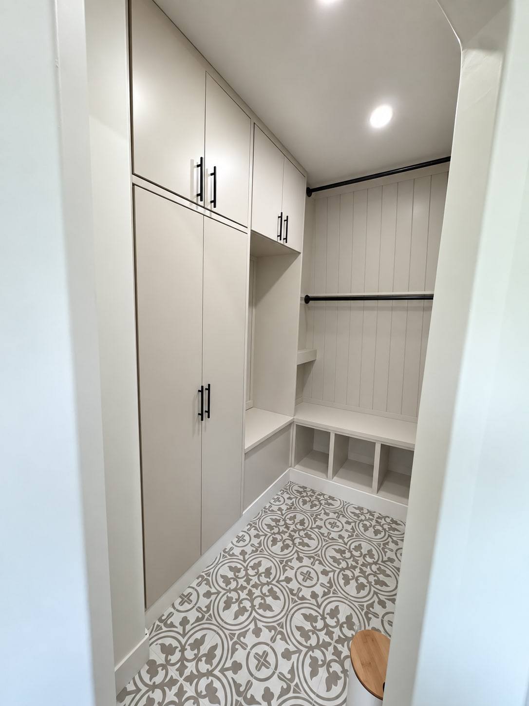 Painted mudroom built-in with tall cabinets, an open bench with cubbies and a beadboard back panel above a patterned tile floor