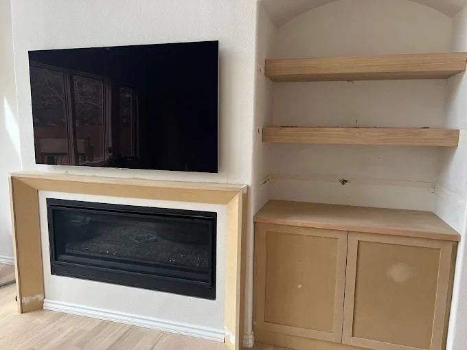 Fireplace surround and TV wall beside floating wood shelves over a low cabinet in an alcove