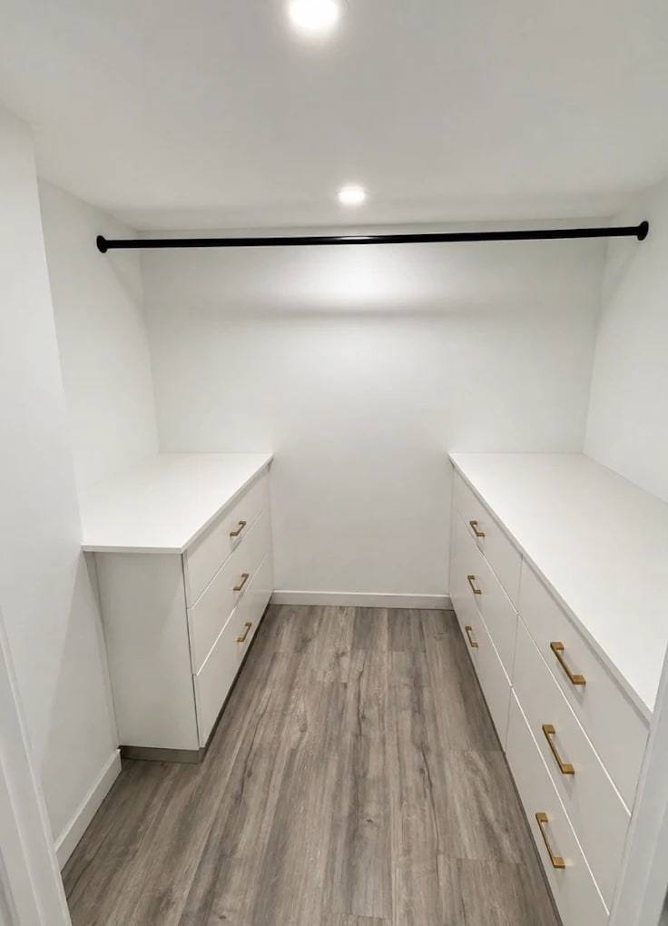 Walk-in closet with two low white dresser built-ins facing each other and a hanging rod above