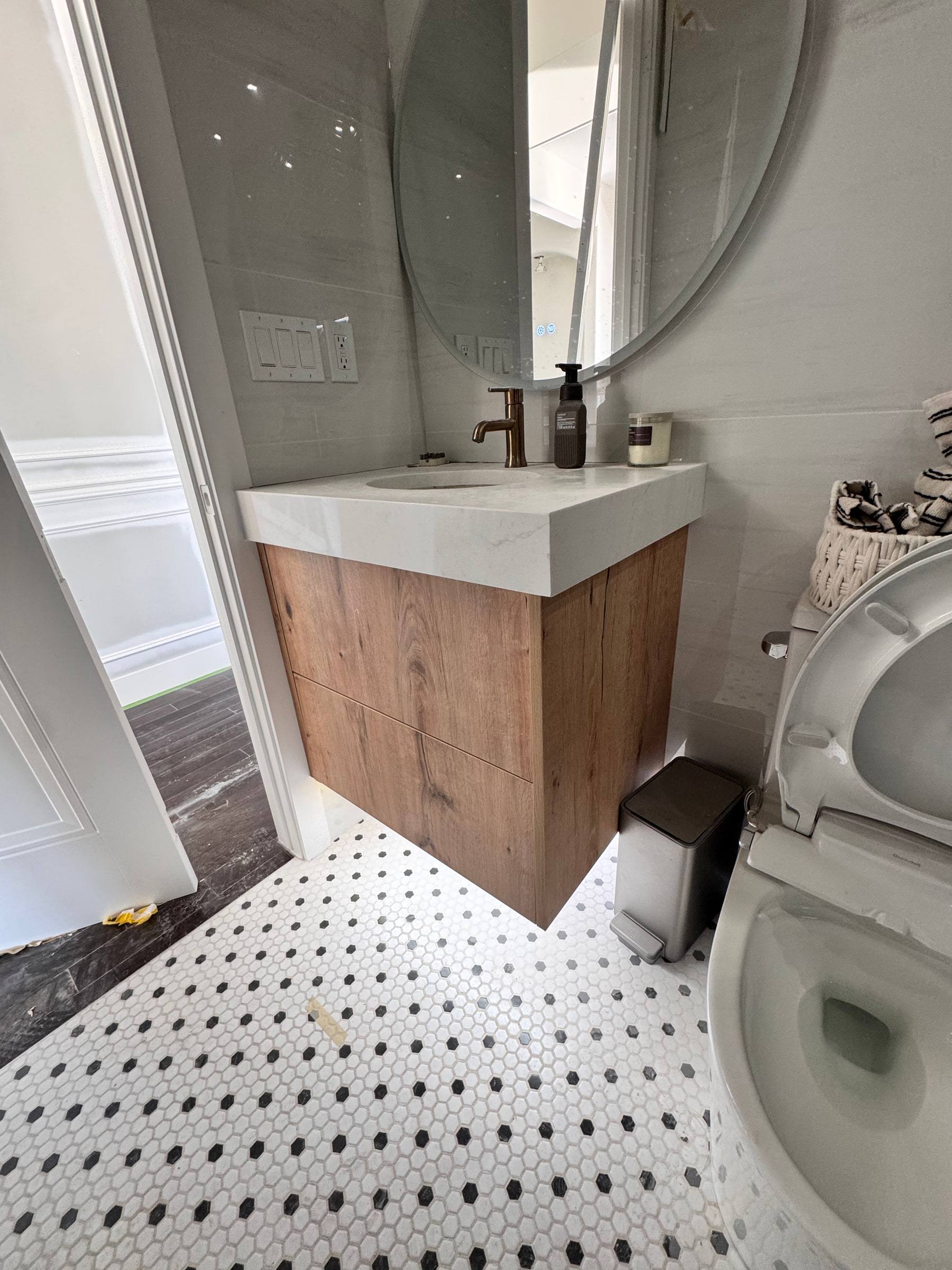 Floating wood vanity with a thick white top in a bathroom with black and white mosaic tile