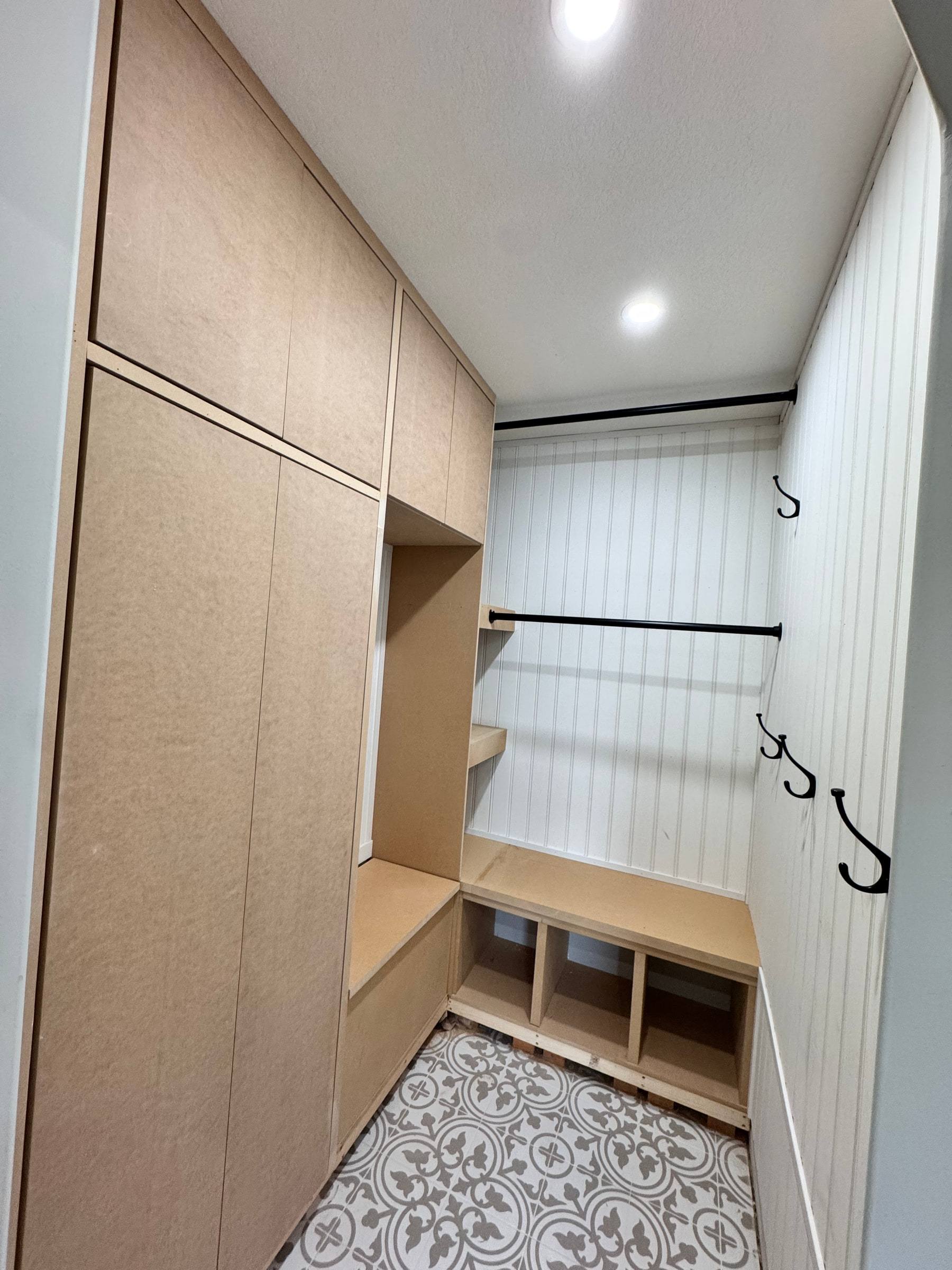 Mudroom built-in installed in raw MDF before painting, with bench, cubbies and coat hooks in place