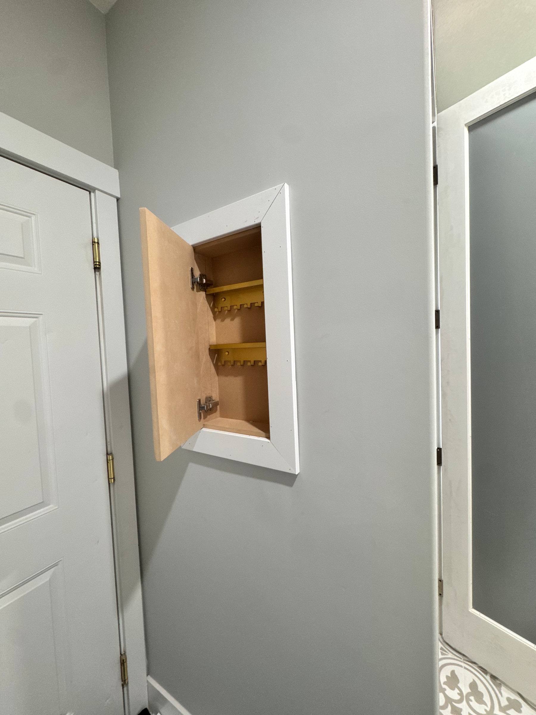 Shallow cabinet built into the wall between two doors, its door open to show the interior